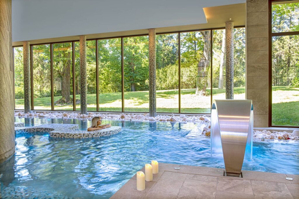 Indoor pool with a large picture window overlooking the park, water jet, and candles at the Bio Spa